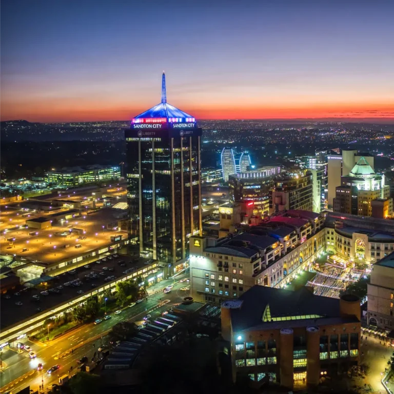 Aerial view of Sandton City in Johannesburg at dusk, with illuminated buildings and city lights—an inspiring setting for team building or exploring affordable team building packages against a colorful sunset sky.