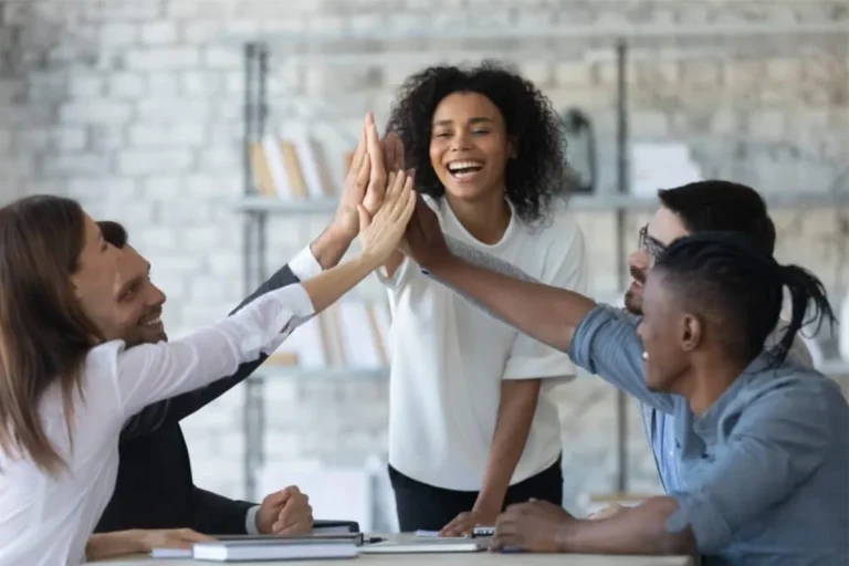 Five happy people giving high-fives around an office table, representing a successful decision to get a quote.