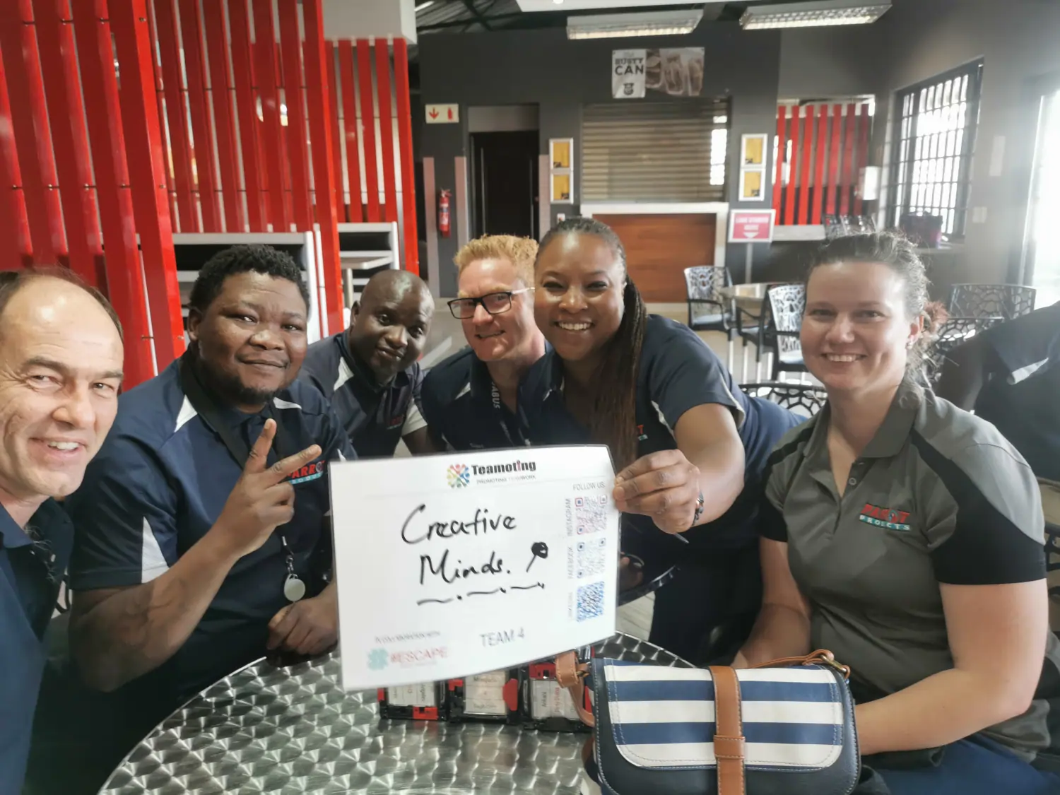 A cheerful team from Parrot Products holding a sign that says "Creative Minds" during team building activities held at their offices