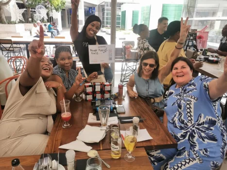 The ABSA team laughing and holding up a "Power Puff Girls" sign during one of the best team building activities at Salsa Mexican Grill in Bedford Centre